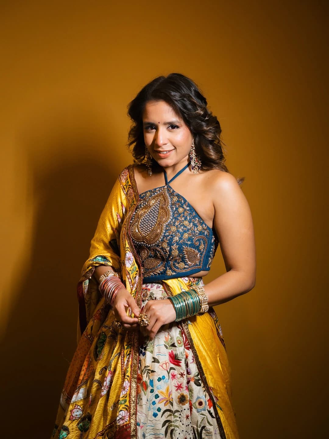 Aishwarya Majmudar in a blue and gold embroidered outfit against a warm studio backdrop