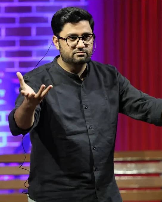 Chirayu Mistry performing in a black shirt and glasses under red and blue stage lighting