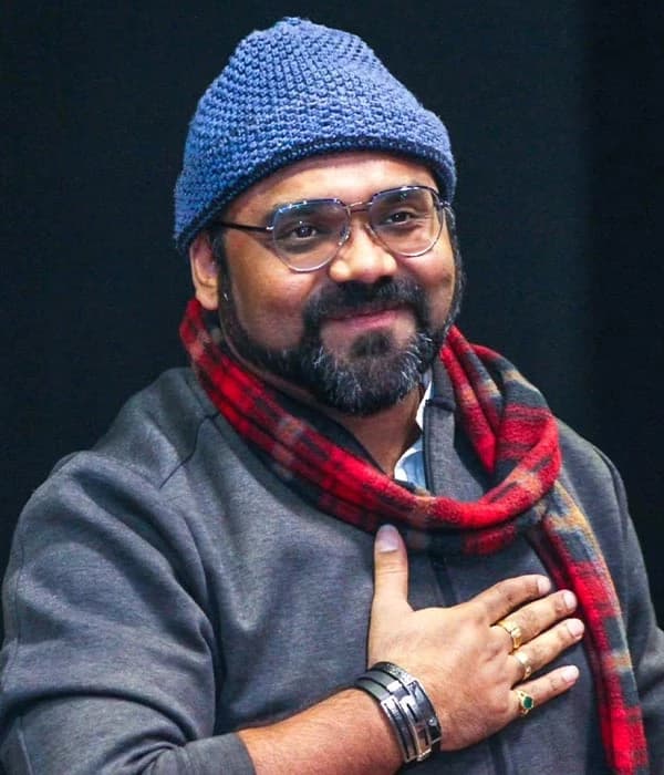 Smit Pandya smiling in glasses, a blue knit cap and a red checked scarf