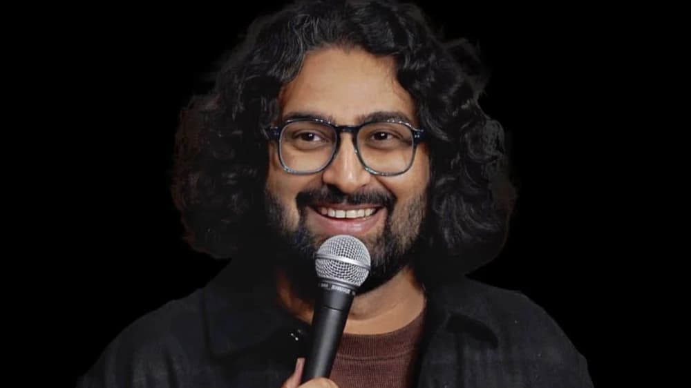 Ravi Gupta smiling into a microphone in glasses, a dark jacket and a brown shirt