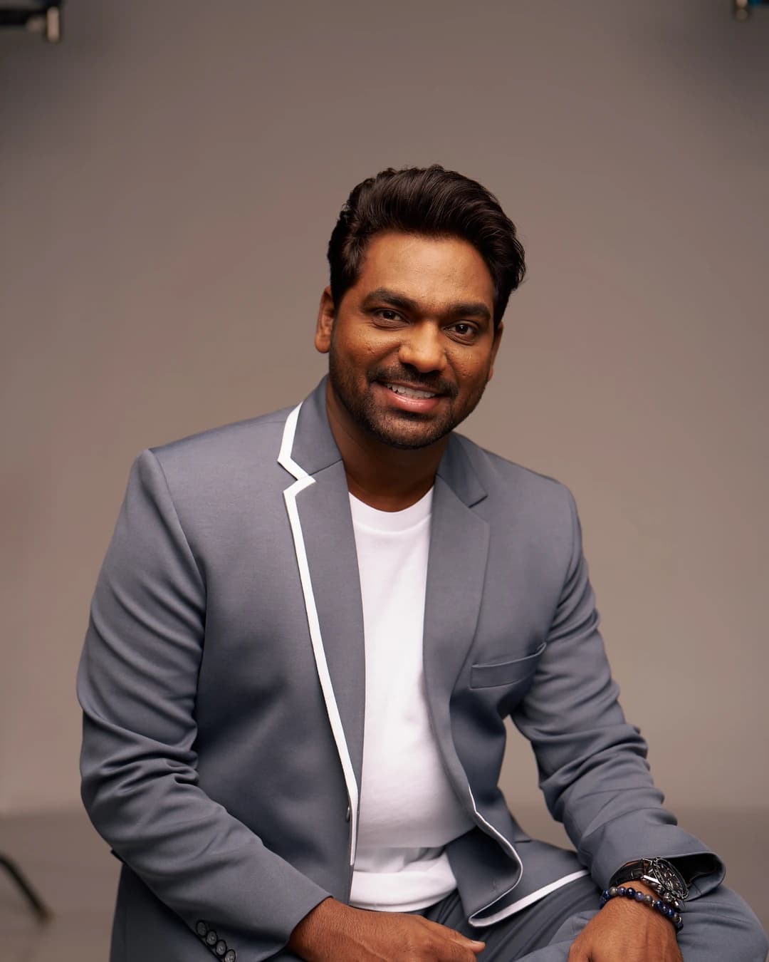 Zakir Khan smiling in a grey blazer and white shirt in a studio portrait